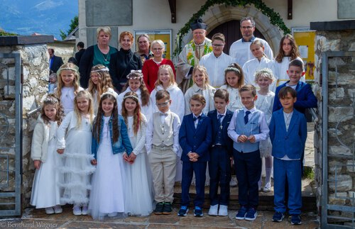 Gruppenfoto der Erstkommunionkinder gemeinsam mit Pfarrer KR Mag. Helmut Mosser, Religionslehrerin Frau Herta Rass (links neben dem Pfarrer), Volksschuldirektorin Frau Petra Perchtold-Weißenegger (neben Frau Rass) und zwei weiteren Volsschullehrerinnen im Eingangsbereich nahe dem Portal der Pfarrkirche Maria Rojach (© Foto: Mag. Bernhard Wagner)