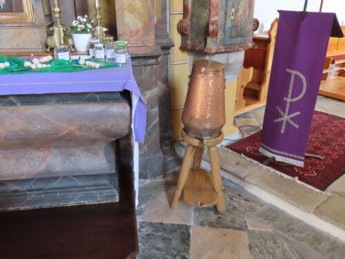 Weihwasserbehälter in der Pfarrkirche Neuhaus mit bereitgestellten Weihwassergefässen am Seitenaltar • Blagoslovljena voda v farni cerkvi na Suhi (Foto: Pfarrarchiv Neuhaus- Suha)