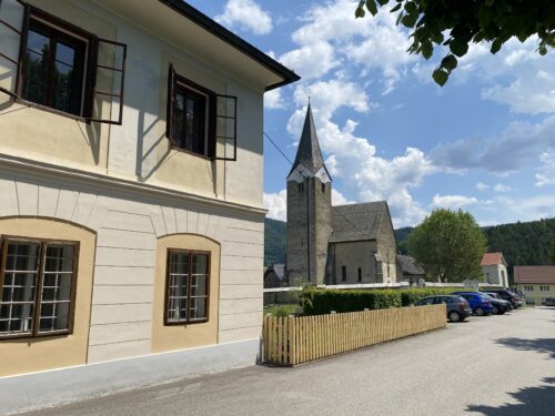 Autos der Taufgemeinschaft vor der Pfarrkirche und dem Pfarrhof Neuhaus • Lep pogled na župnišče in na farno cerkev (Foto: Pfarrarchiv Neuhaus- Suha)