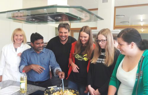 Gemeinsames Zubereiten von indischen Speisen als “ganzheitliches Lernen mit allen Sinnen“ (im Bild: Pfarrer Mula mit Klassenvorstand Helga Pacher, Diakon Huber u. Schülerinnen der 4C der NMS Ferlach). (© Foto: Pfarre Ferlach/Borovlje)